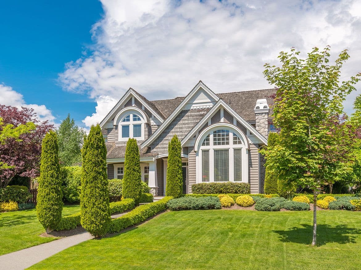 Front of a two storey house with arched windows, clipped hedges and a mown lawn