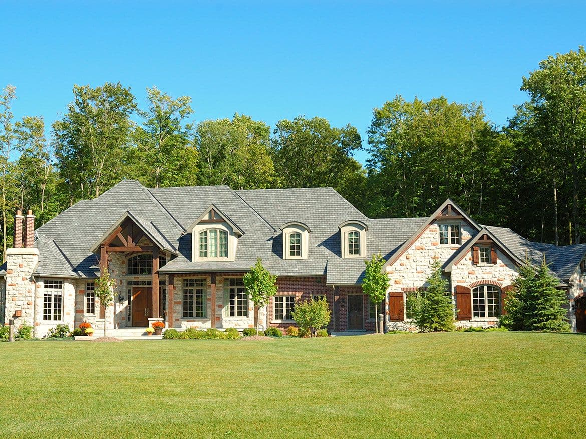 Wide stone and brick home with several gables set behind a large green lawn