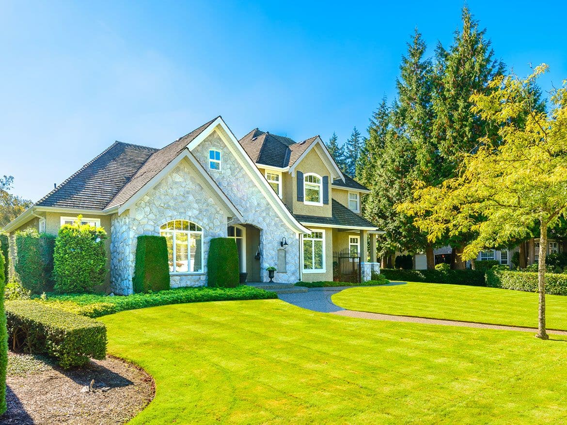Stone fronted home with arched windows, shaped hedges and a curved garden path