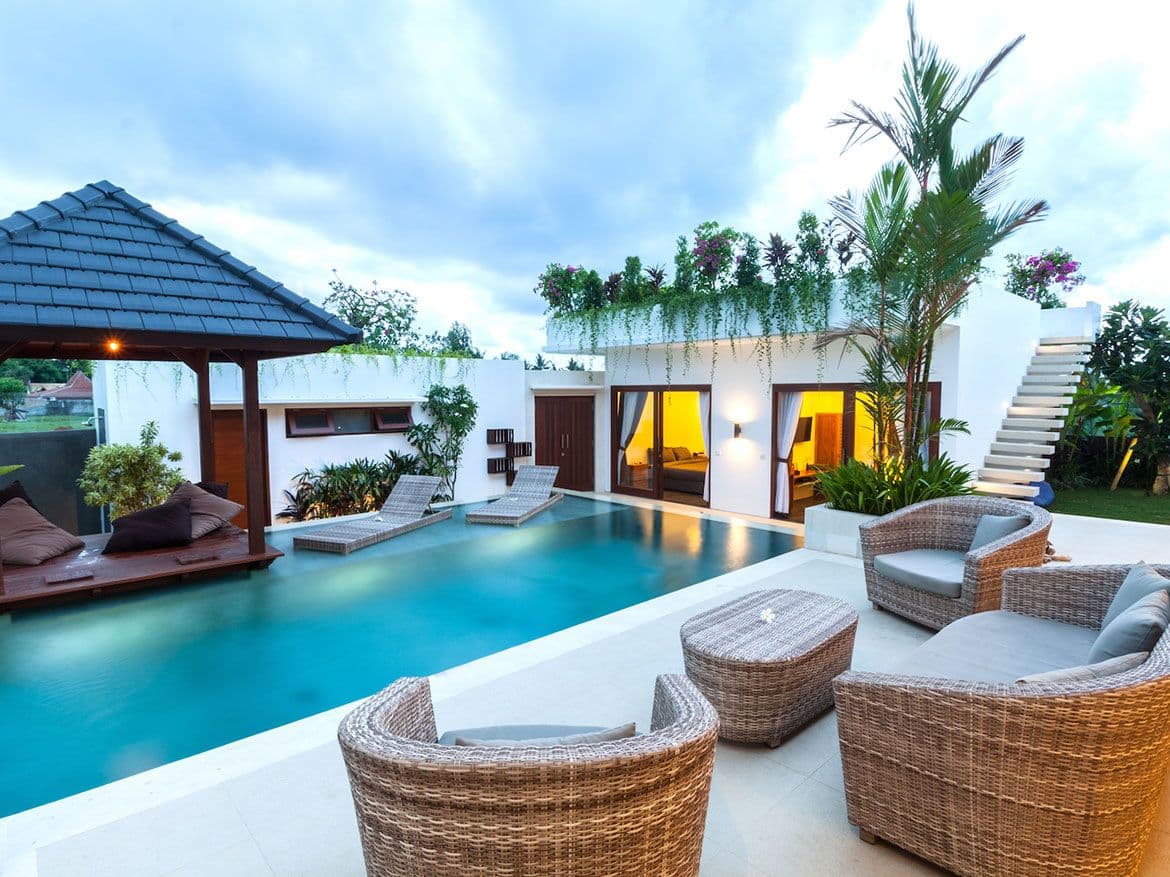 Villa with a swimming pool, covered lounge, sun loungers and wicker chairs at dusk